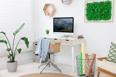 Green artificial plant wall panel and desk with computer in light room. Interior design