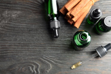 Photo of Bottles with essential oil and cinnamon sticks on black wooden table, flat lay. Space for text