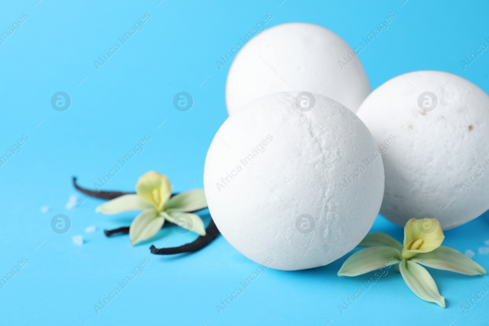 Photo of White bath bombs, vanilla sticks and flowers on light blue background, closeup. Space for text