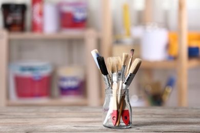 Glass jar with paint brushes on wooden table in workshop. Space for text