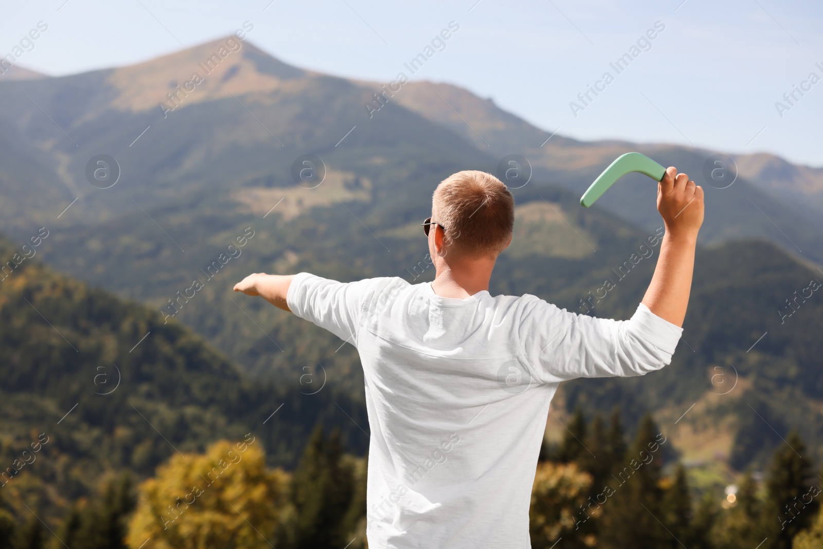 Photo of Man throwing boomerang in mountains on sunny day, back view