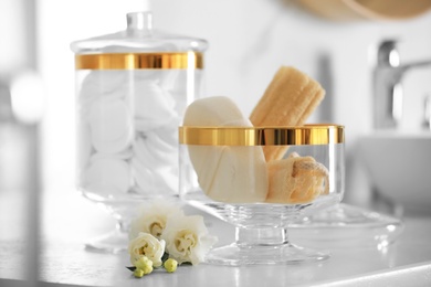 Photo of Jars with cotton pads and loofah sponges on countertop in bathroom