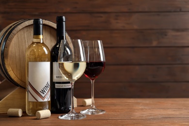 Photo of Glasses with delicious wine, bottles and barrel on table