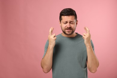 Photo of Emotional man crossing his fingers on pink background, space for text