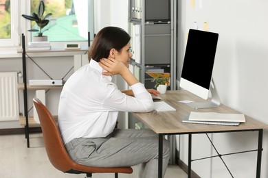 Photo of Young woman with bad posture sitting at workplace in office. Symptom of scoliosis