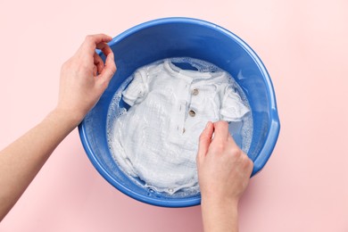 Photo of Woman washing baby clothes in basin on pink background, top view