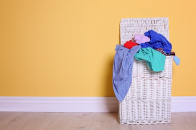 Photo of Laundry basket with dirty clothes on floor near color wall