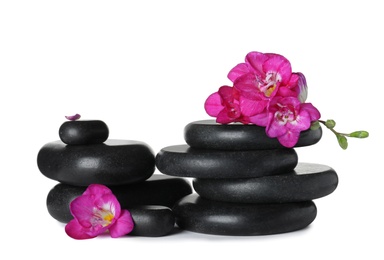 Stack of black spa stones and fresh flowers isolated on white