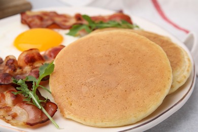 Photo of Plate with tasty pancakes, fried egg, arugula and bacon on light table, closeup