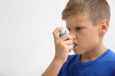 Little boy using asthma inhaler on light background