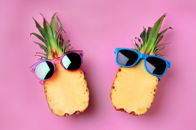 Photo of Funny pineapples with sunglasses on color background