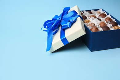 Photo of Box of delicious chocolate candies on light blue background, space for text