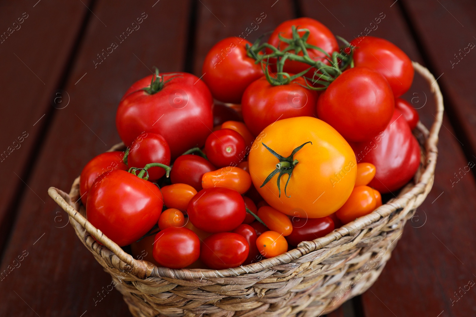 Photo of Wicker basket with fresh tomatoes on wooden table, closeup