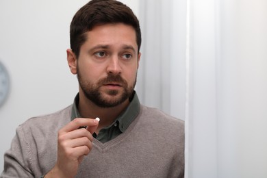 Depressed man taking antidepressant pill indoors, space for text