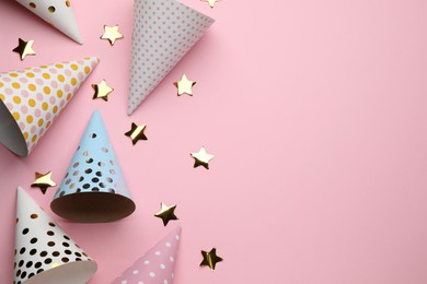 Photo of Bright party hats and shiny confetti on pink background, flat lay. Space for text