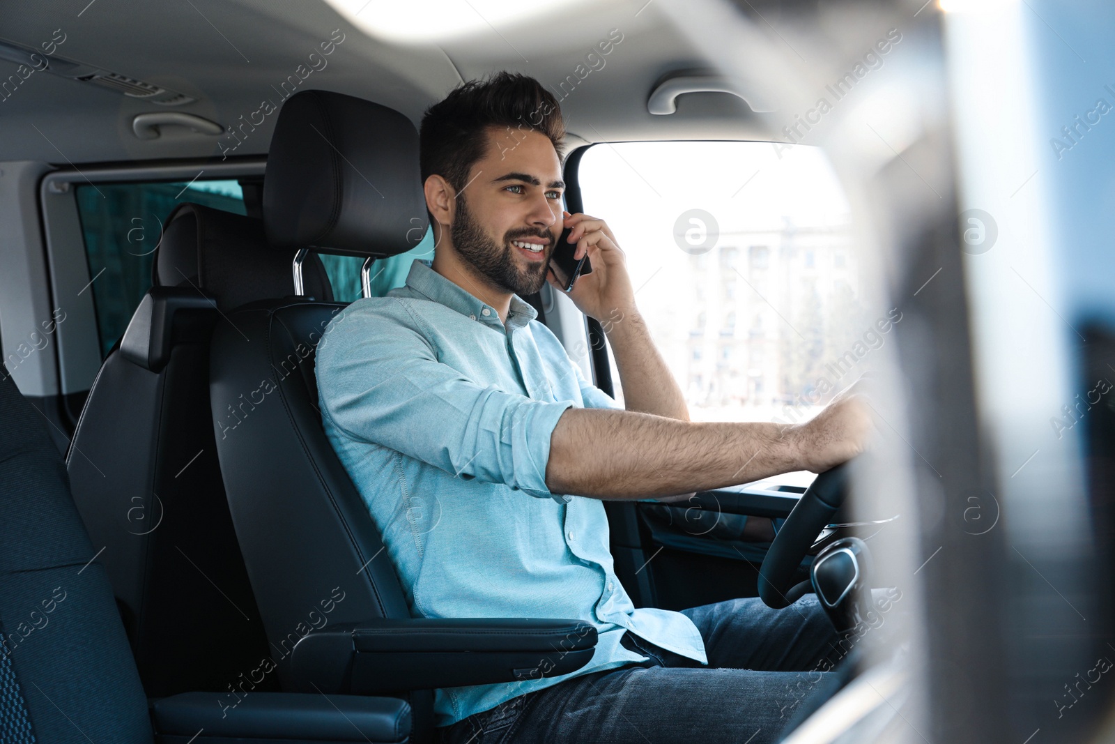 Photo of Handsome young man talking on smartphone while driving his car