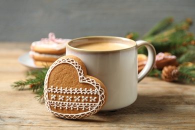 Photo of Tasty heart shaped gingerbread cookie and hot drink on wooden table