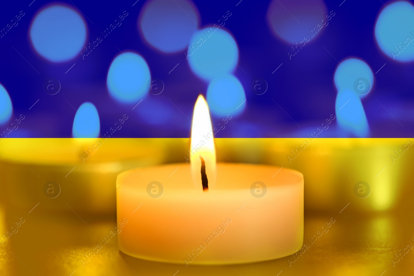 Image of Burning candle and Ukrainian national flag on background, closeup