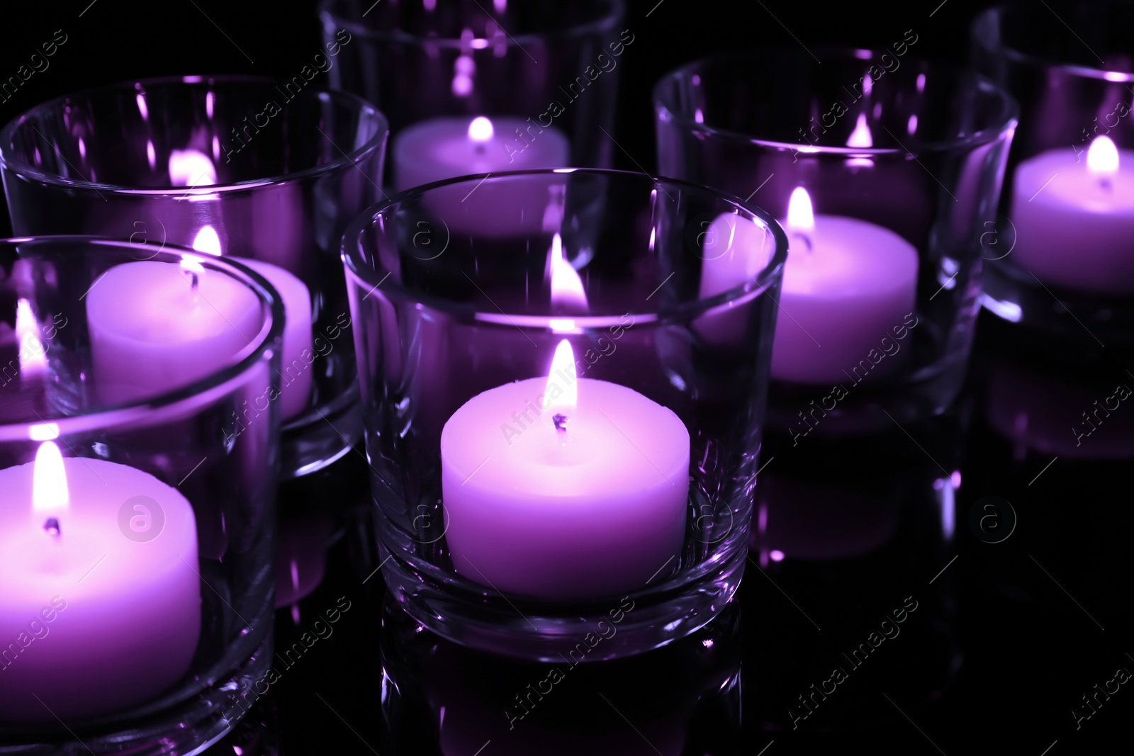 Image of Beautiful burning violet candles on black background, closeup. Funeral attributes