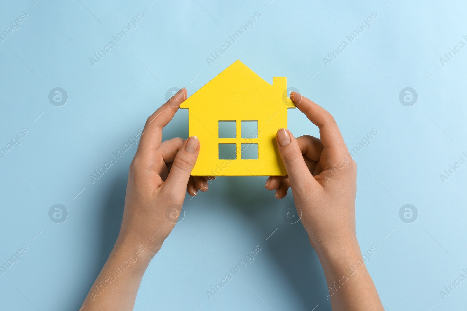 Photo of Woman holding house figure on light blue background, top view