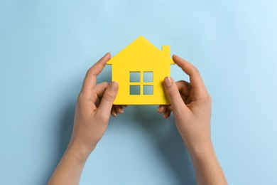 Photo of Woman holding house figure on light blue background, top view