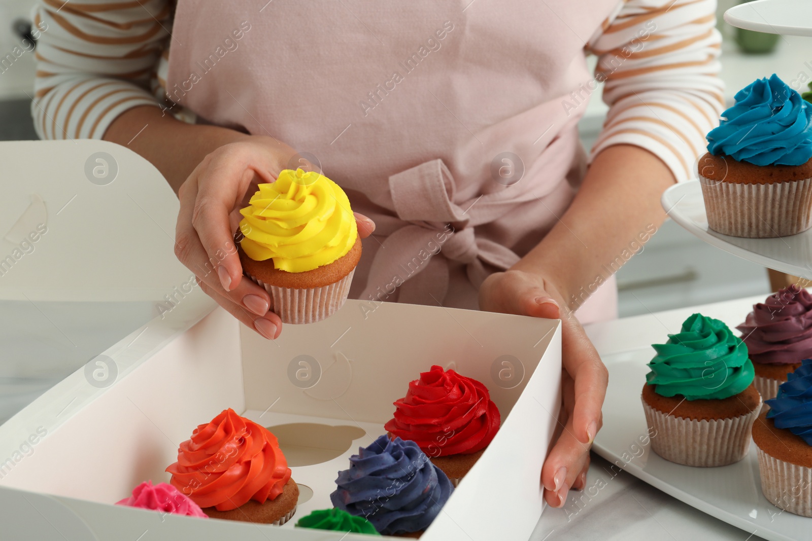 Photo of Woman with box of delicious colorful cupcakes at white table indoors, closeup