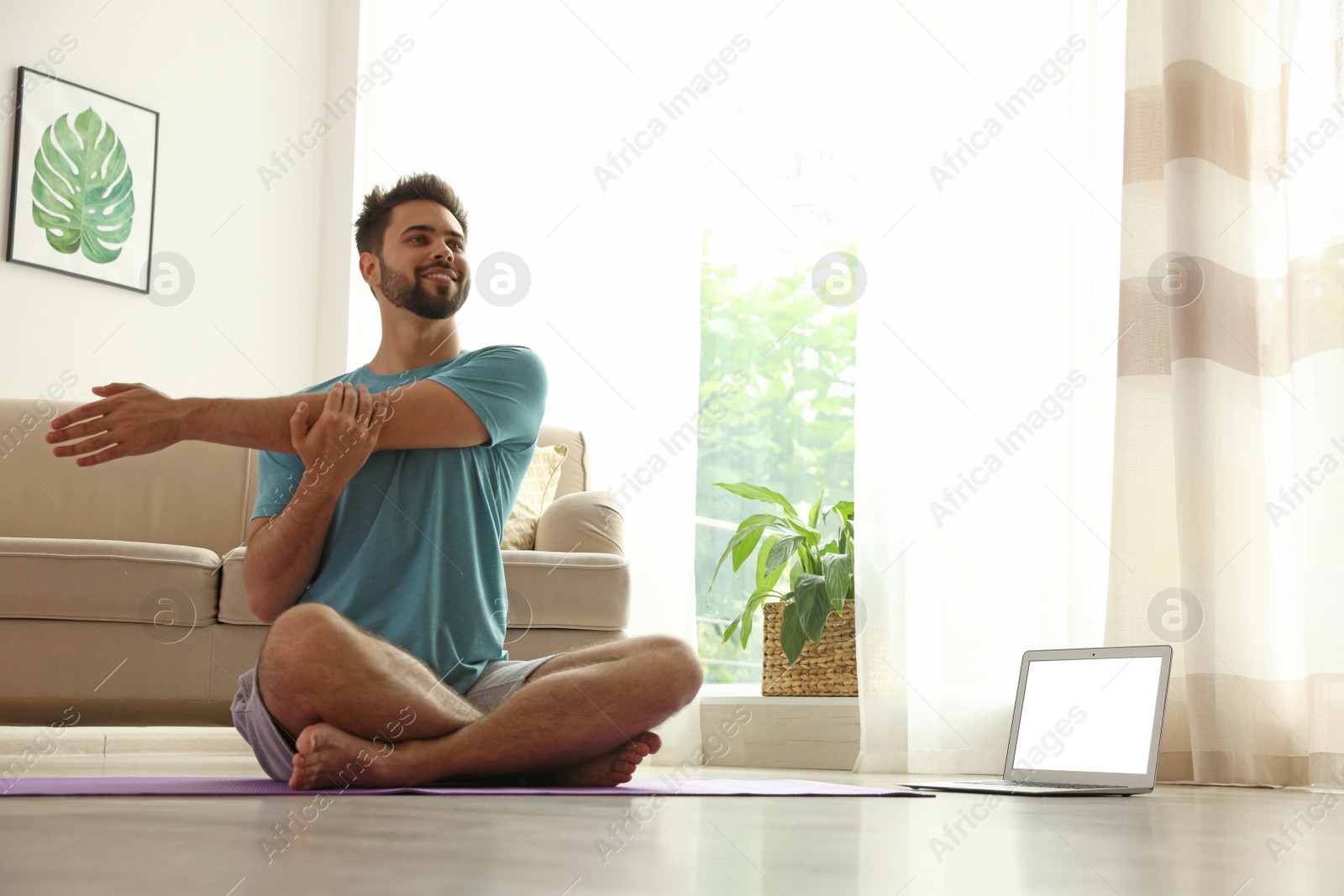 Photo of Man practicing yoga while watching online class at home during coronavirus pandemic. Social distancing