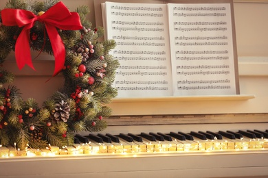 Photo of White piano with decorative wreath and note sheets closeup. Christmas music