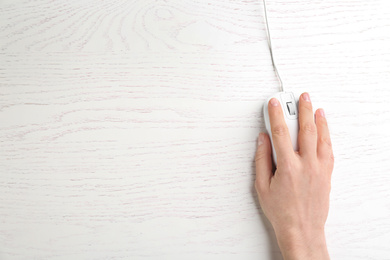 Photo of Woman using modern wired optical mouse on white wooden table, top view. Space for text