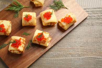 Delicious thin pancakes with red caviar on wooden table, top view