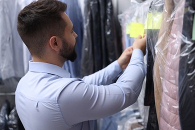 Dry-cleaning service. Worker sticking paper note onto clothes indoors