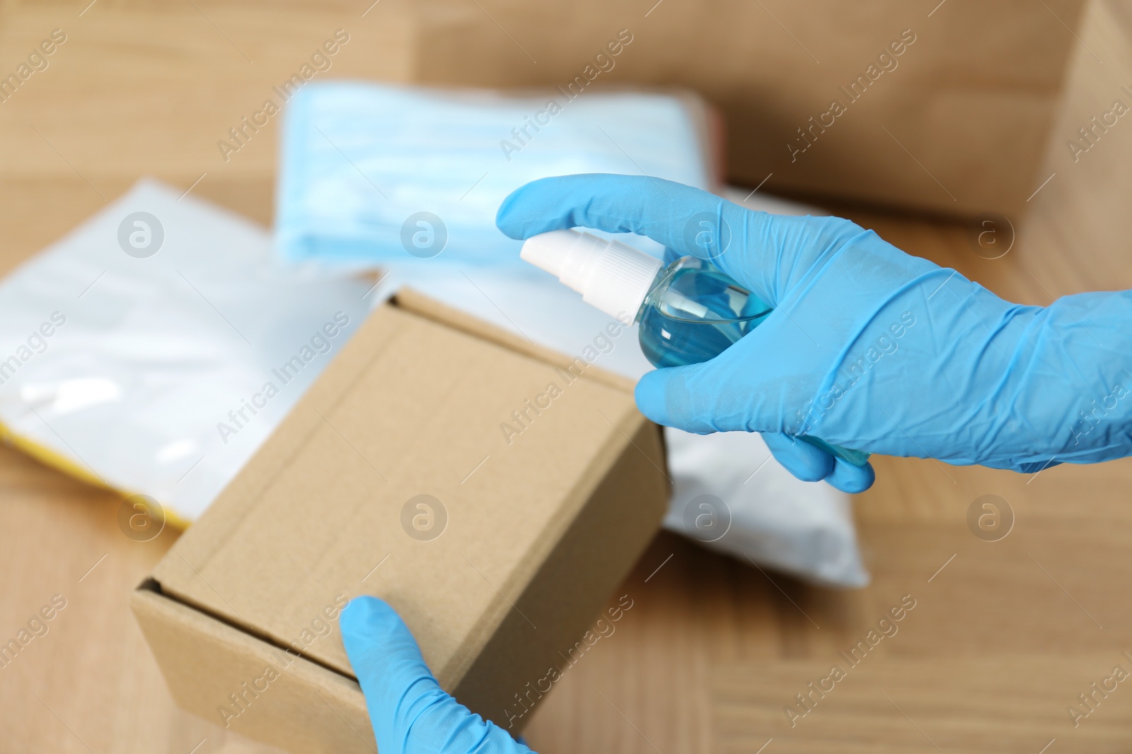 Photo of Woman spraying antiseptic onto parcel at wooden table, closeup. Preventive measure during COVID-19 pandemic
