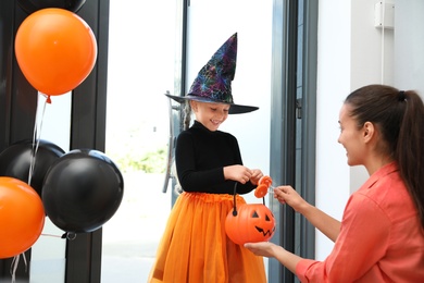 Photo of Cute little girl dressed as witch trick-or-treating at doorway. Halloween tradition