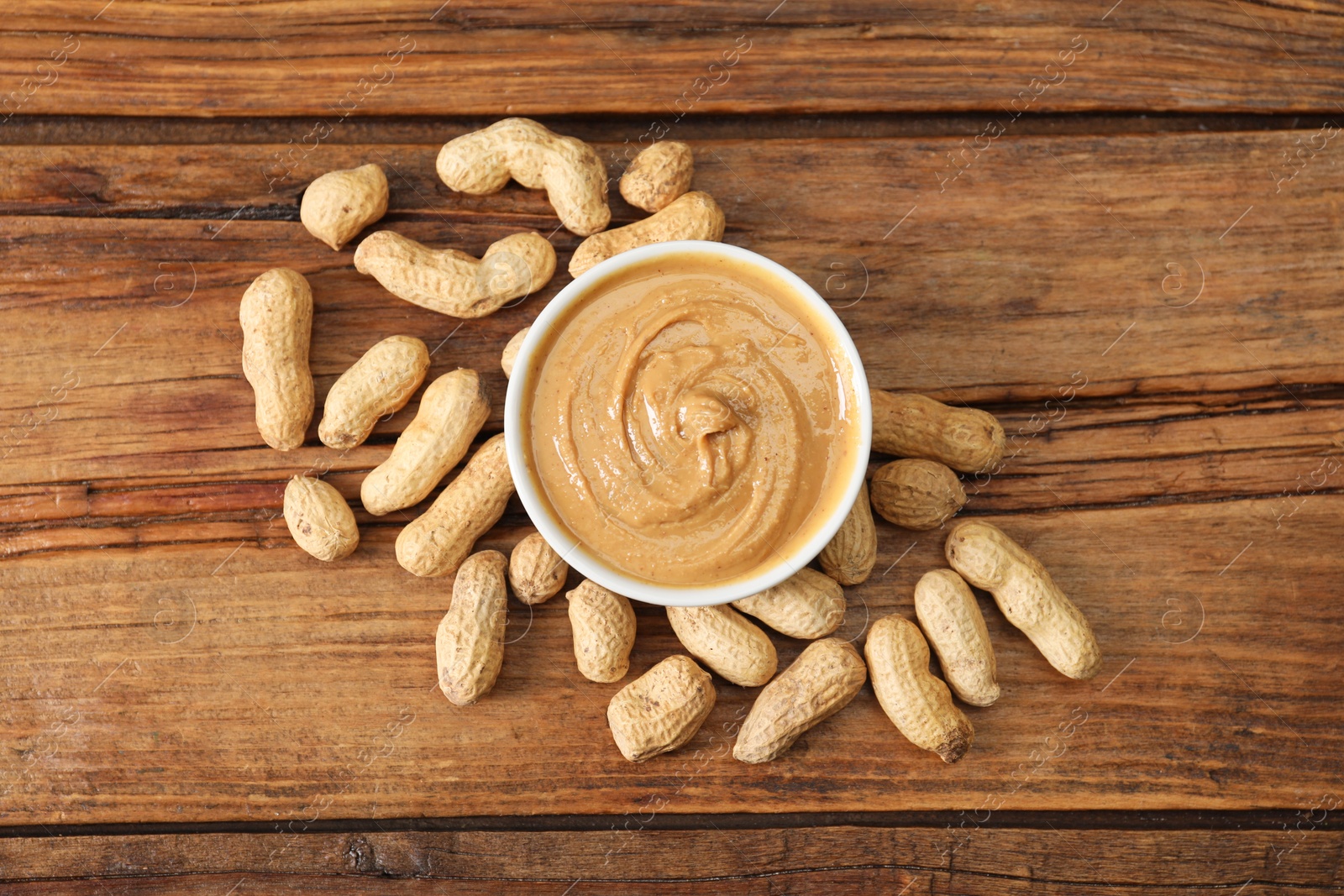 Photo of Delicious nut butter in bowl and peanuts on wooden table, top view