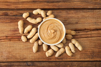 Delicious nut butter in bowl and peanuts on wooden table, top view