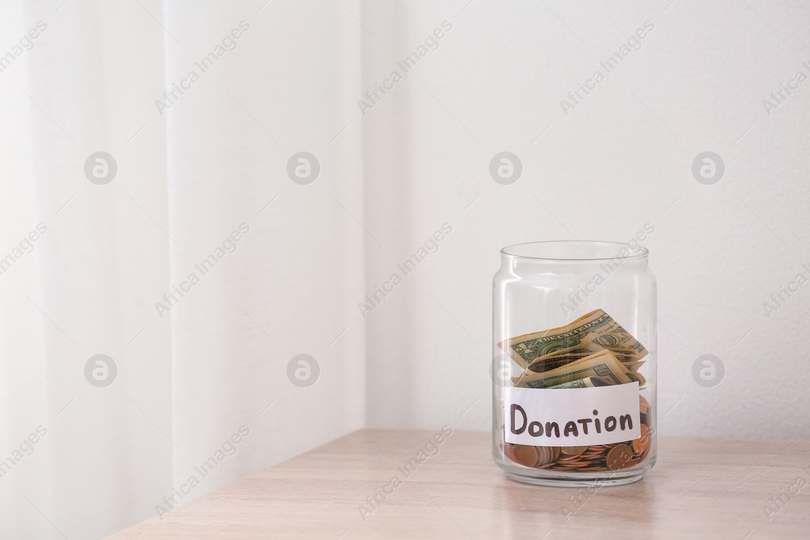 Photo of Glass jar with money and label DONATION on table against light background. Space for text