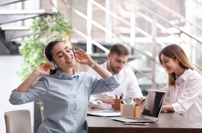 Photo of Young businesswoman with headphones, laptop and her colleagues at table in office