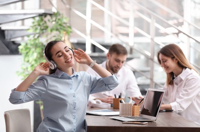 Young businesswoman with headphones, laptop and her colleagues at table in office