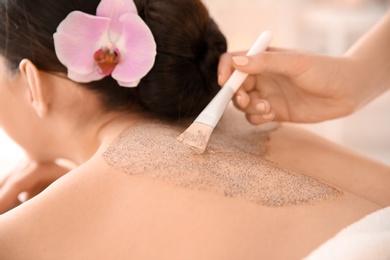 Photo of Beautiful young woman having massage with body scrub in spa salon