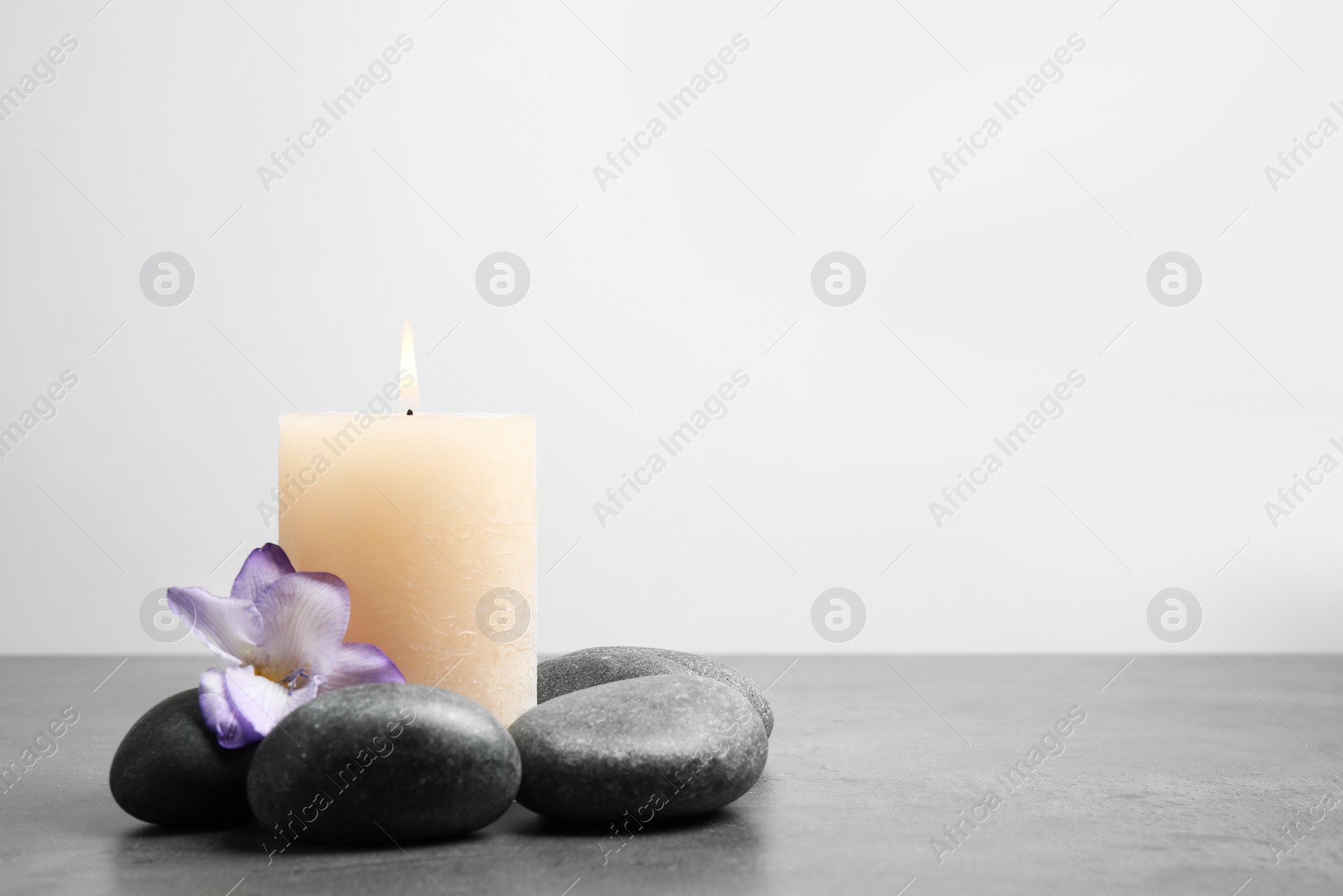 Photo of Spa stones, burning candle and freesia flower on grey table, space for text