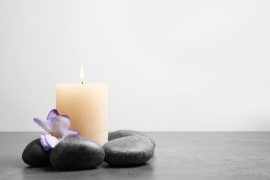 Spa stones, burning candle and freesia flower on grey table, space for text