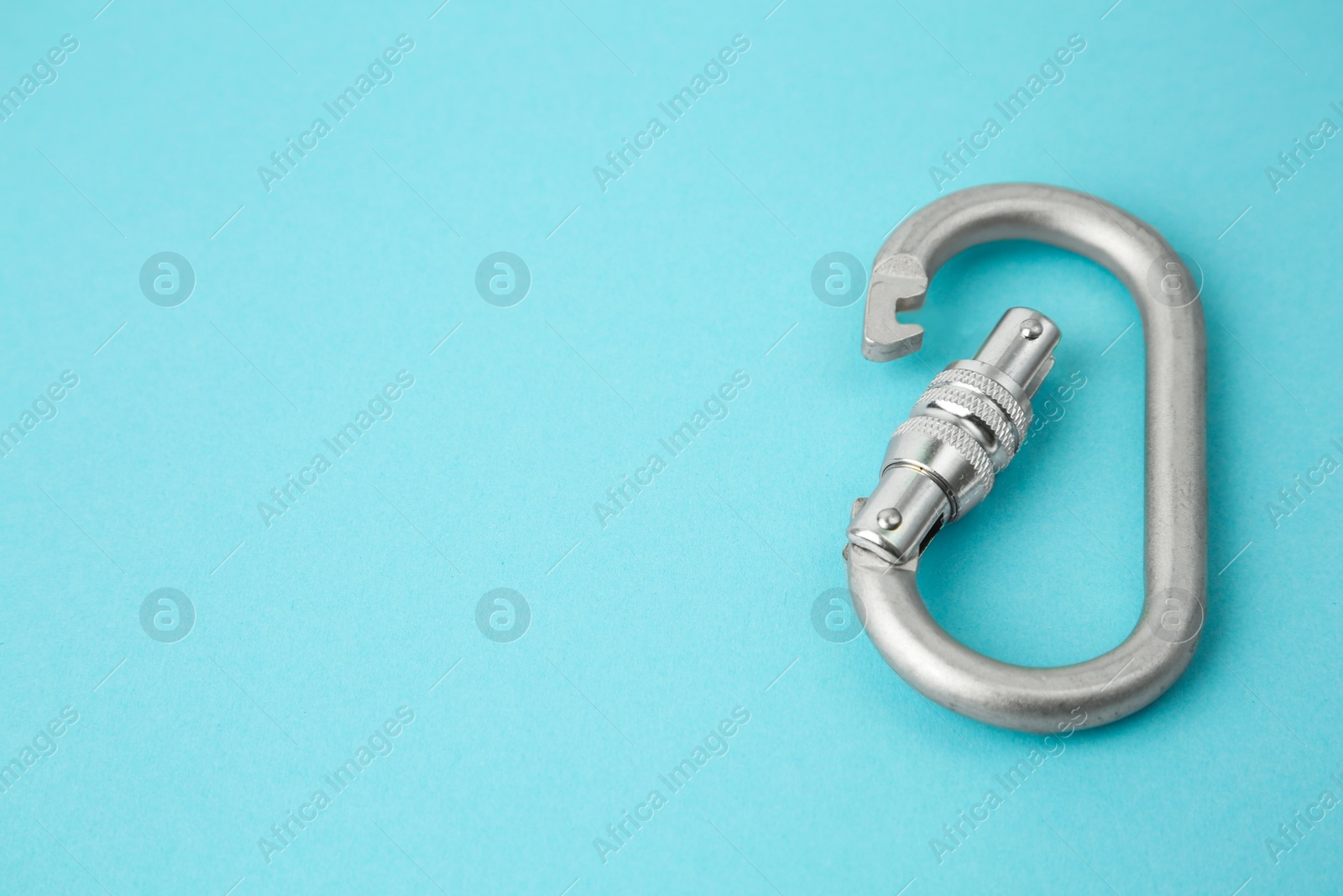 Photo of One metal carabiner on light blue background, closeup. Space for text