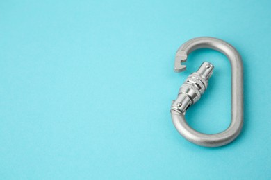 Photo of One metal carabiner on light blue background, closeup. Space for text