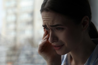 Sad young woman crying near window indoors, closeup with space for text. Loneliness concept