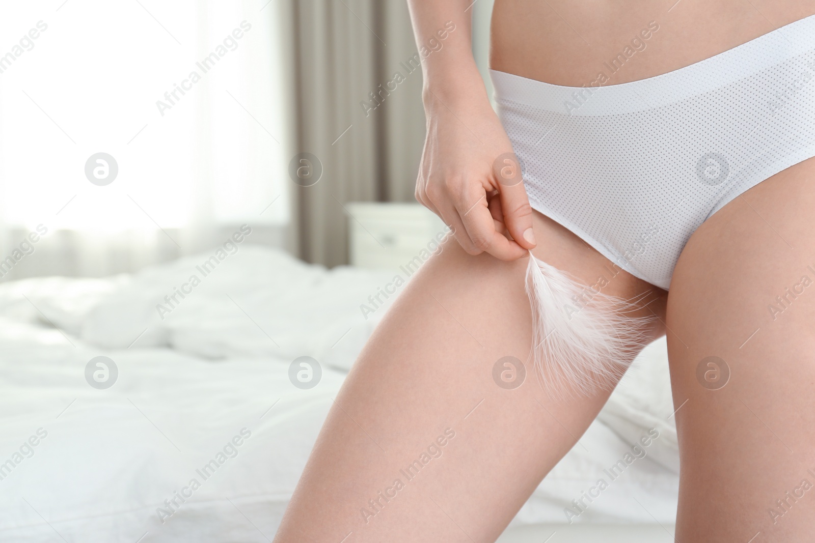 Photo of Closeup of young woman touching leg with feather in bedroom, space for text. Epilation procedure