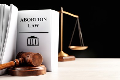 Abortion law book, gavel and scales of justice on white table against black background