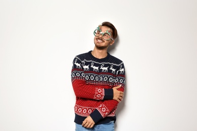 Young man in Christmas sweater with party glasses on white background