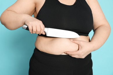 Photo of Obese woman with knife on light blue background, closeup. Weight loss surgery