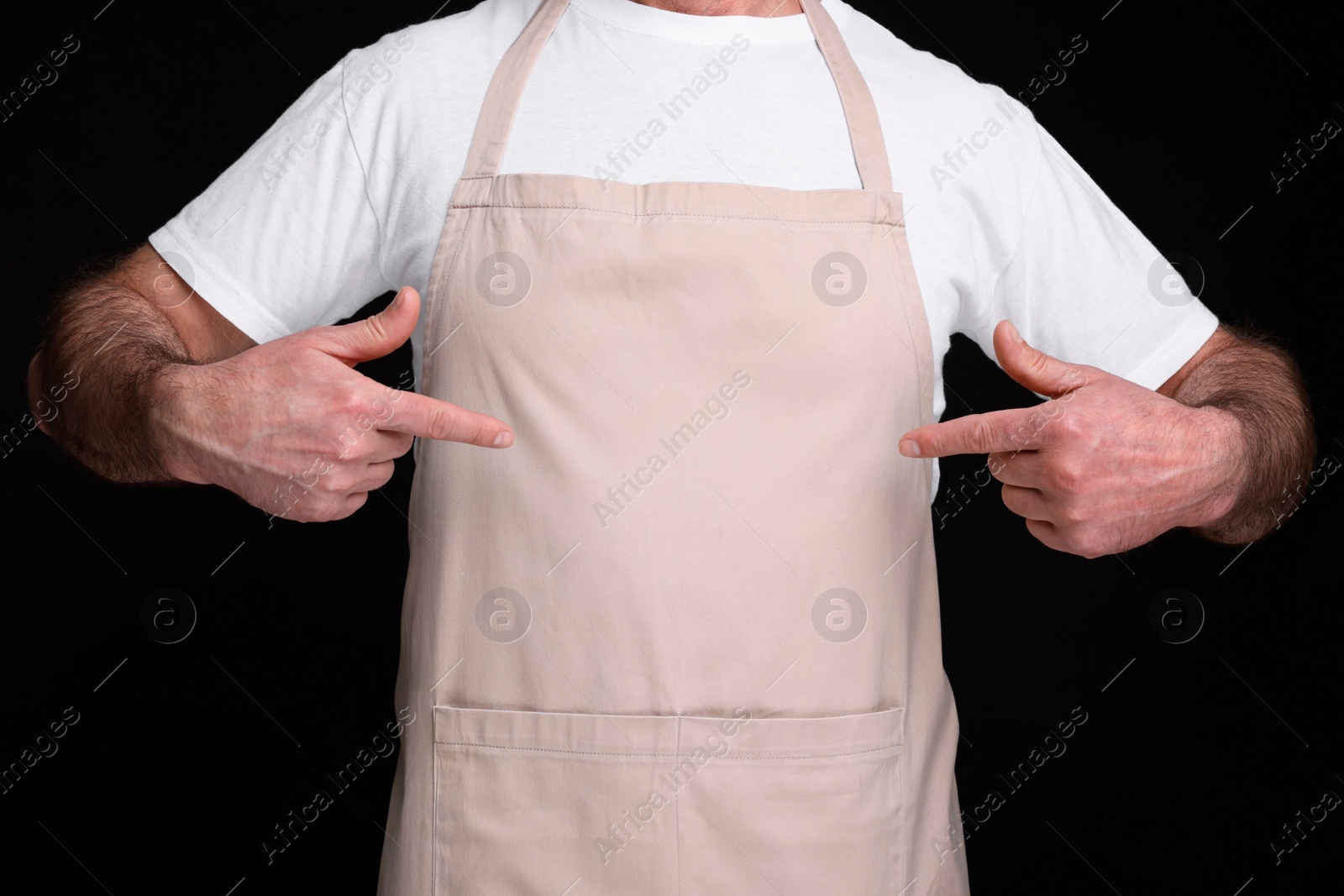 Photo of Man pointing at kitchen apron on black background, closeup. Mockup for design