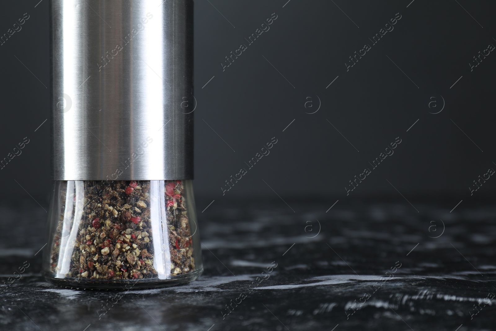 Photo of Pepper shaker on dark marble table, closeup. Space for text